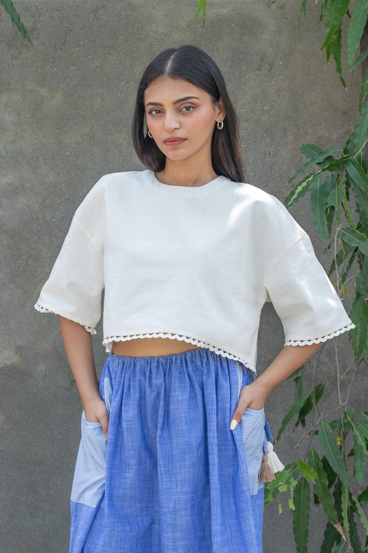 Woman wearing a white top and blue skirt against a gray wall with greenery.